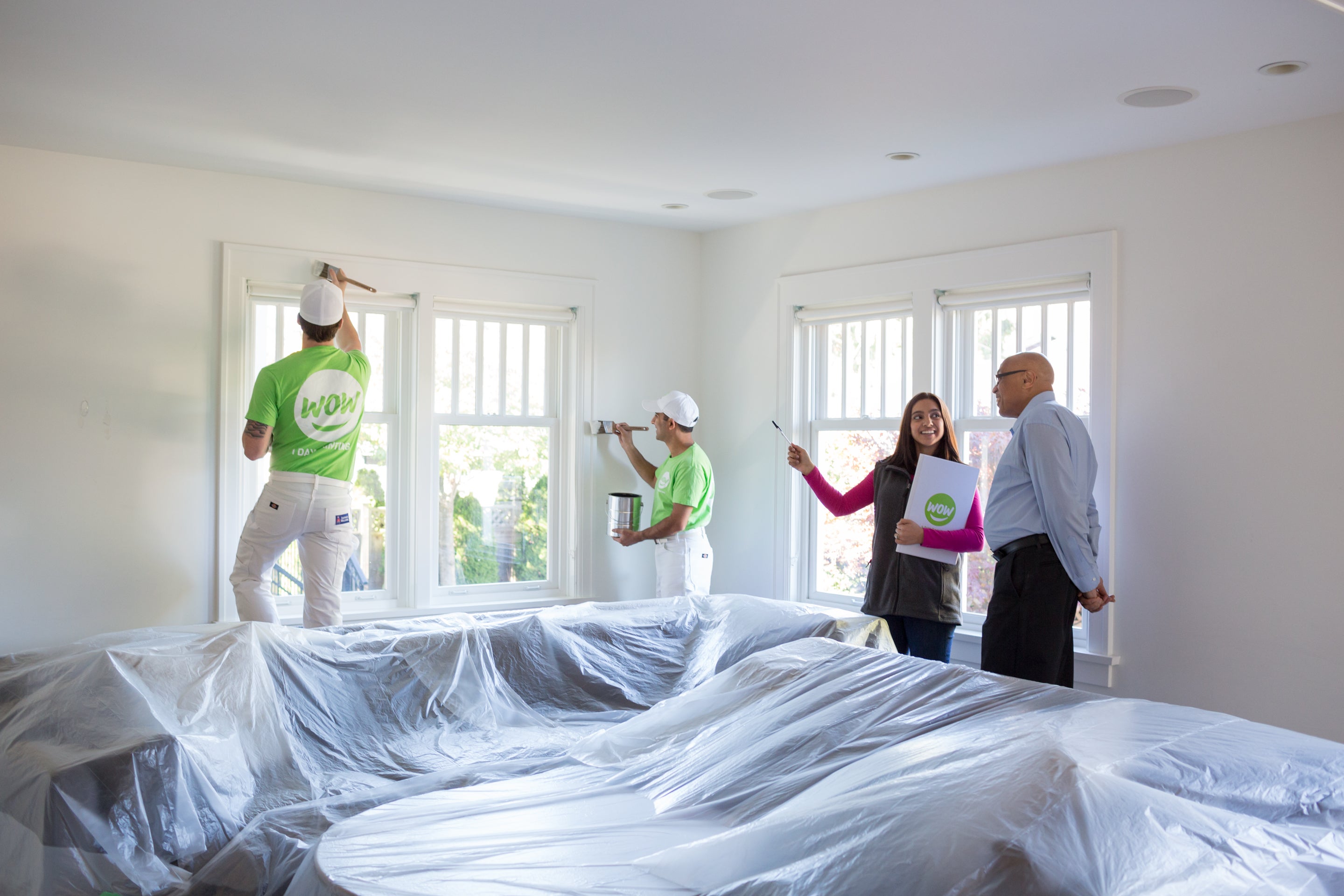 wow1daypainting happy employees in uniform painting home interior with customer watching