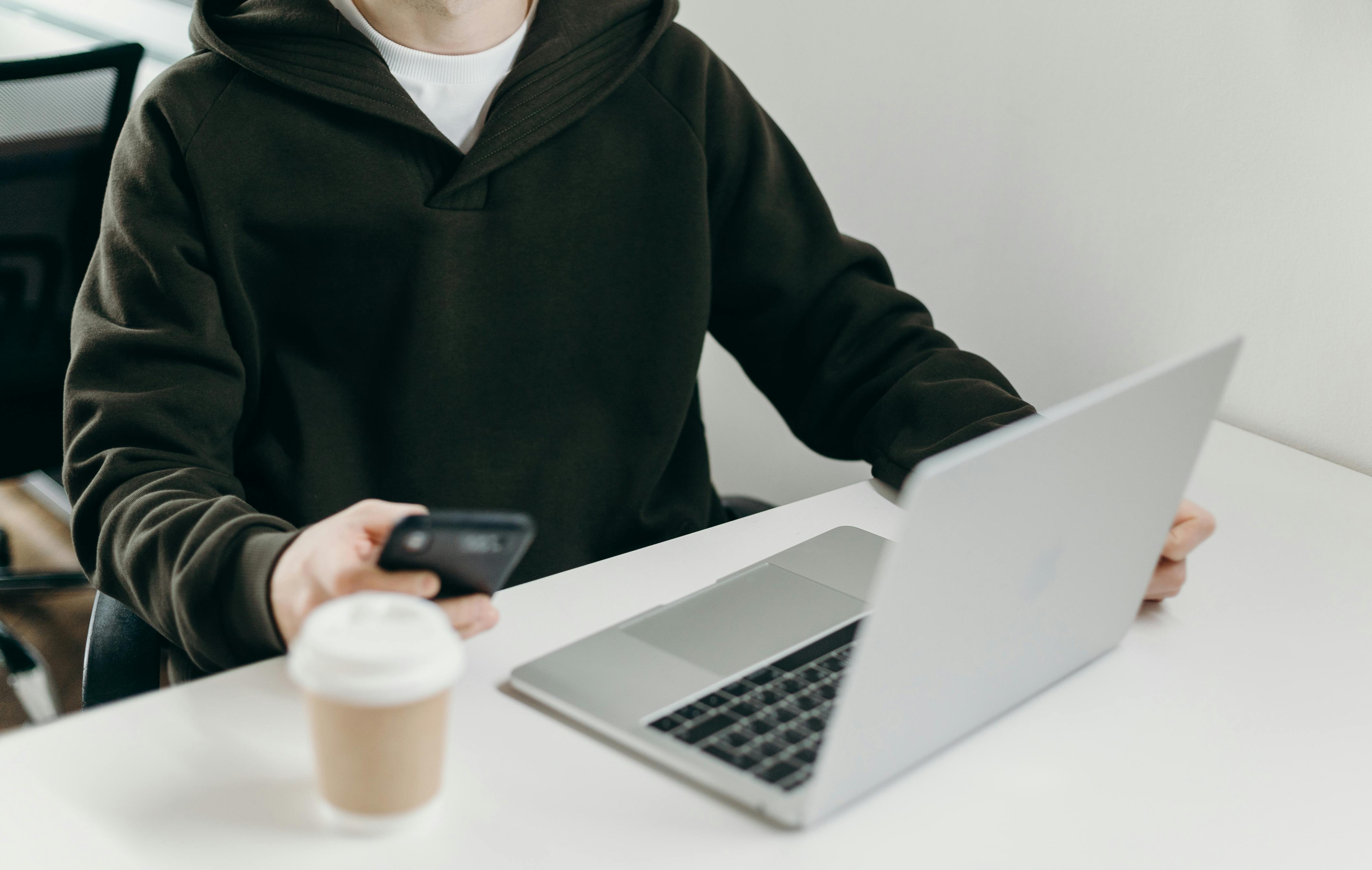 man working from laptop with phone in hand and coffee